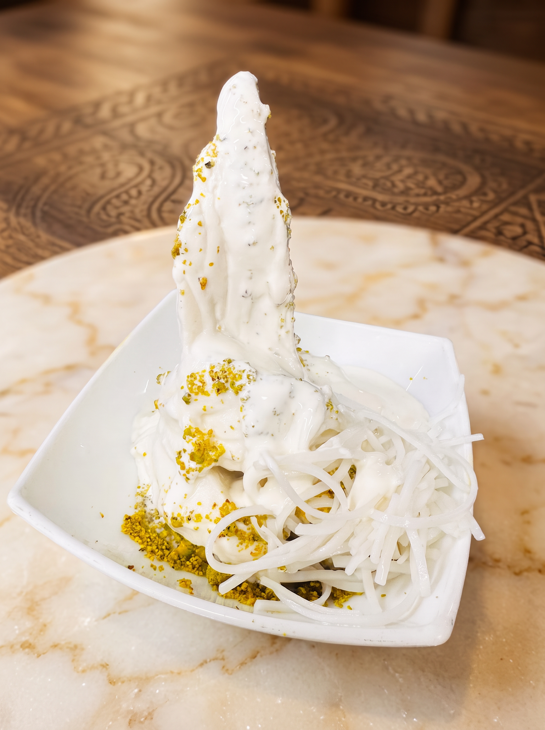 Bowl of handmade Afghan sheer yakh topped with crushed pistachios and falooda noodles